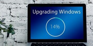 A laptop screen showing 'Upgrading Windows' at 14% on a desk with a white brick wall backdrop illustrating Unlock the Secrets: SEO Best Practices for Effective Content Updates.