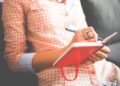 Person in a plaid shirt writing in a red notebook planning tasks, Master Your Website Maintenance Schedule: Boost Performance Now!