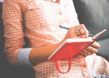 Person in a plaid shirt writing in a red notebook planning tasks, Master Your Website Maintenance Schedule: Boost Performance Now!