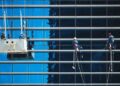 High-rise window cleaners suspended on ropes cleaning a reflective blue glass façade, illustrating Essential WordPress maintenance tips to keep your site thriving.