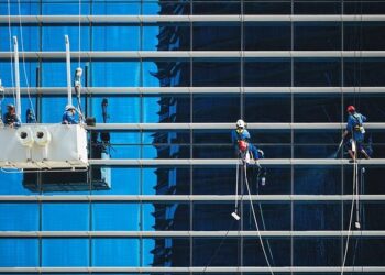 High-rise window cleaners suspended on ropes cleaning a reflective blue glass façade, illustrating Essential WordPress maintenance tips to keep your site thriving.