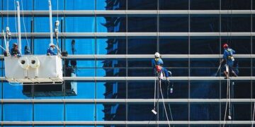 High-rise window cleaners suspended on ropes cleaning a reflective blue glass façade, illustrating Essential WordPress maintenance tips to keep your site thriving.