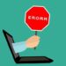 A hand reaches from a laptop holding a red stop sign reading ERORR as a visual reminder to Avoid These Common Website Backup Mistakes That Could Cost You Big.