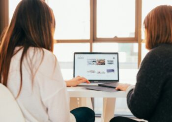 Two people seated at a bright table viewing a laptop screen with an online product catalog, Discover the best website backup solutions for beginners today!