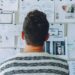 Person standing in front of a wall of pinned website sketches and notes to Boost Your Small Business Success with a Website Maintenance Plan.