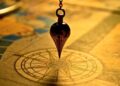 A pendulum hanging over a compass on warm parchment, suggesting direction and focus to Choose the Best Website Maintenance Provider for Ultimate Success.