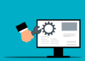 A hand holding a wrench toward a desktop monitor with a gear icon illustrating Essential website maintenance tips every beginner must know now.