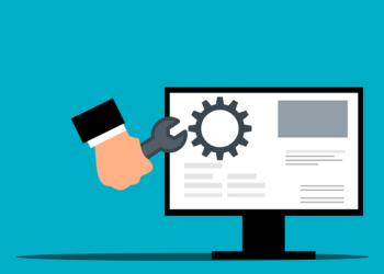 A hand holding a wrench toward a desktop monitor with a gear icon illustrating Essential website maintenance tips every beginner must know now.